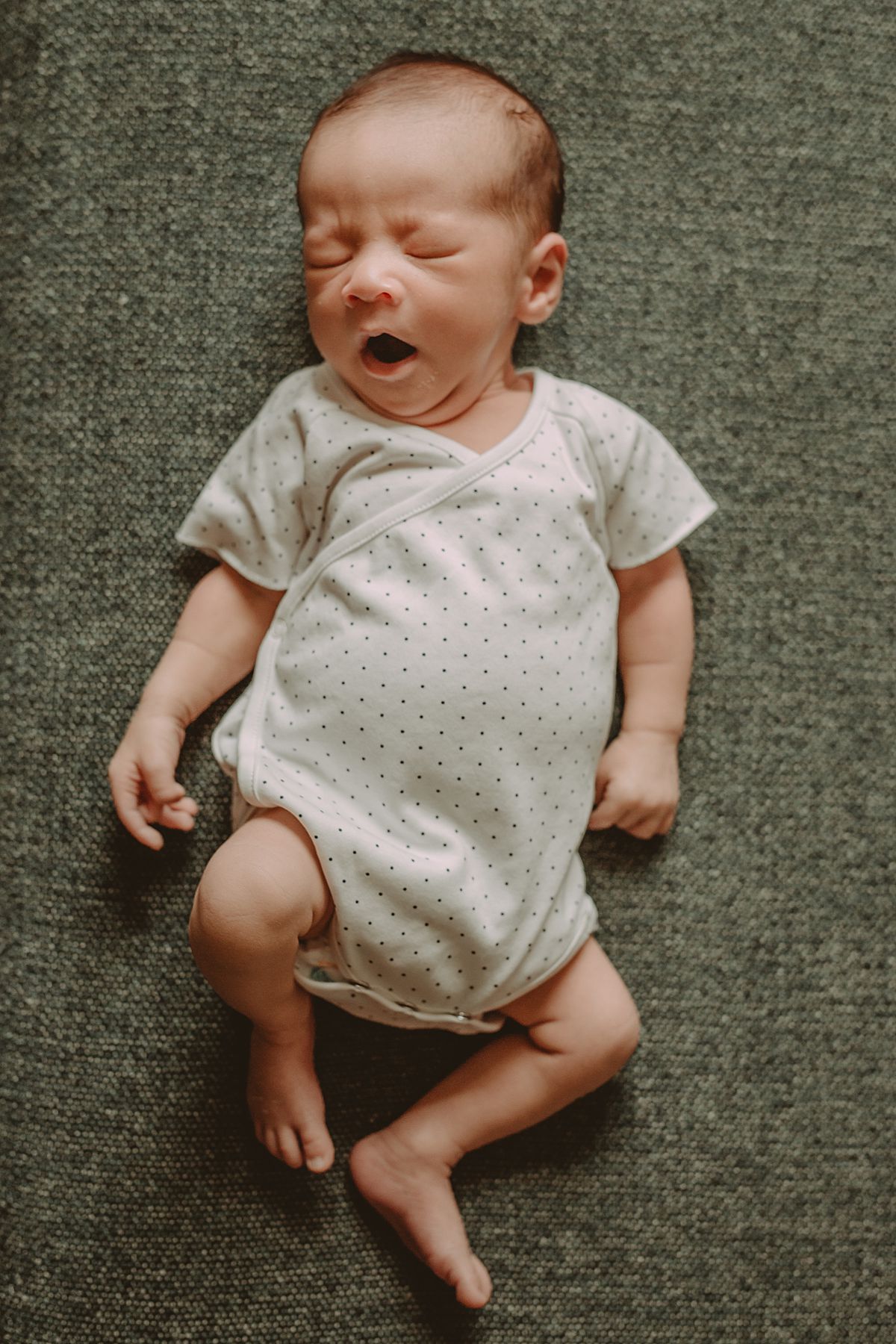 newborn son yawns while laying on couch during documentary newborn photo session in nyc apartment
