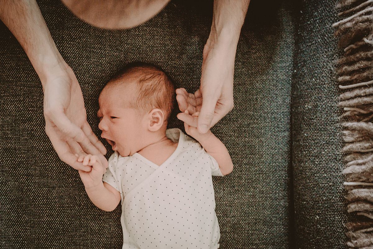 dad plays with son's hands while son lays on couch in living room of nyc apartment