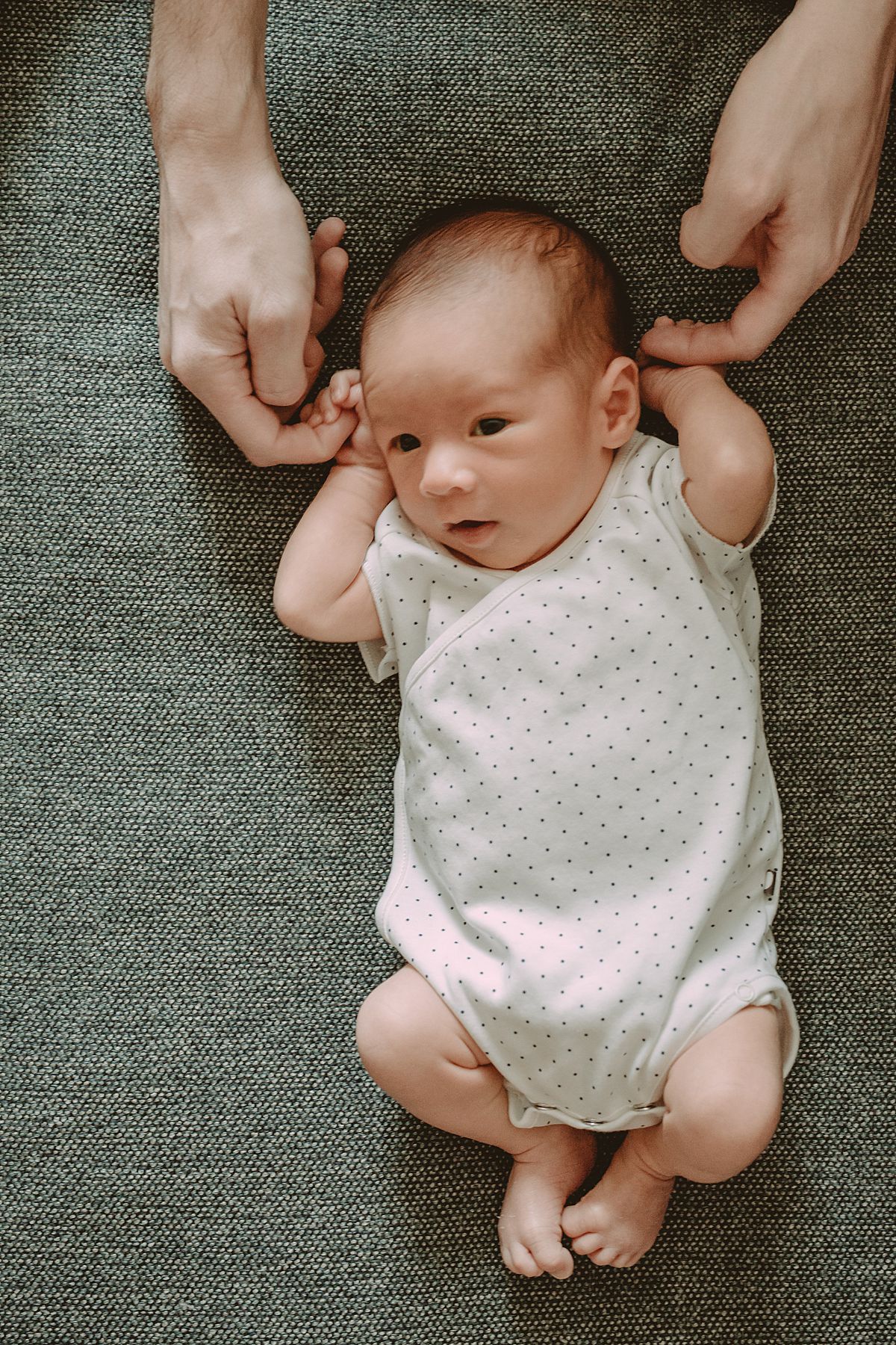dad plays with newborn son's hands while son lays on the couch during nyc family newborn session in manhattan