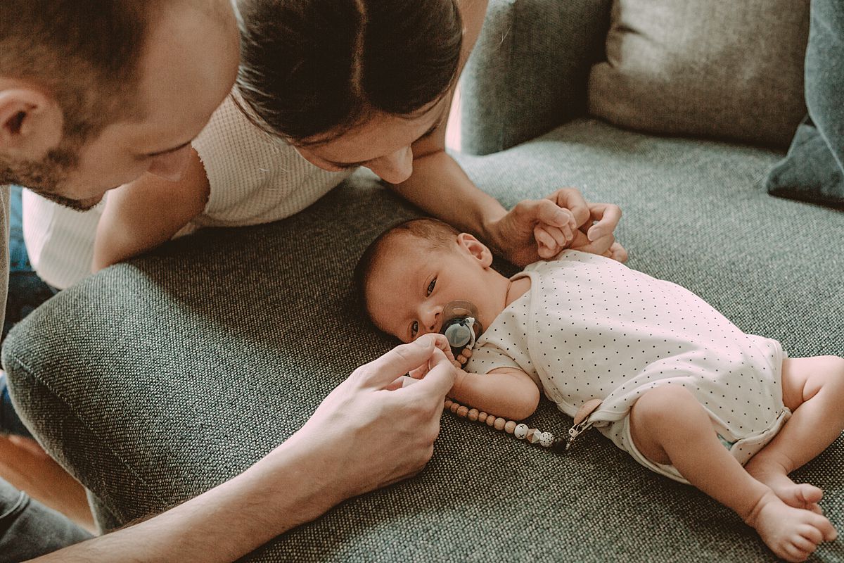nyc newborn photographer takes photo of mom and dad playing with son's hands while he lays on the couch