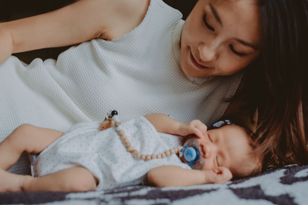 image of mom and newborn son laying on bed on black and white rug during nyc family lifestyle session