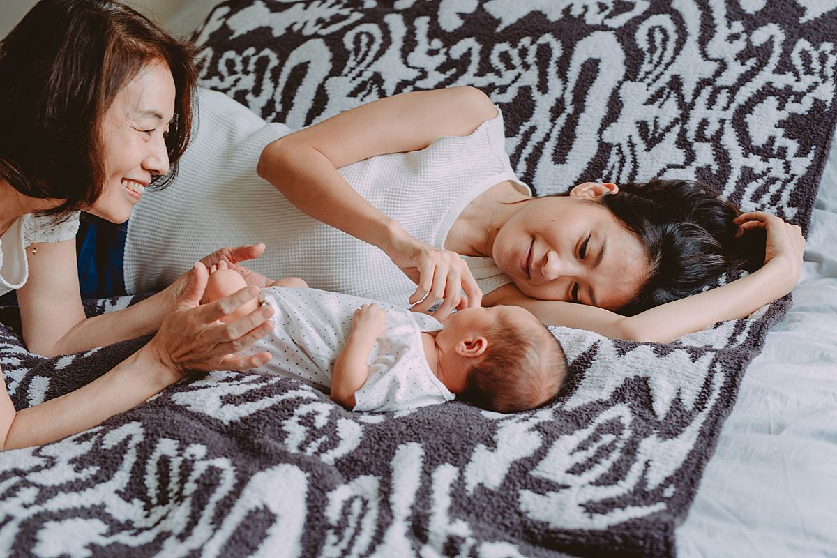 image of mom, grandma and newborn son laying on bed on black and white rug during nyc family lifestyle session. photo from krystil mcdowall photography