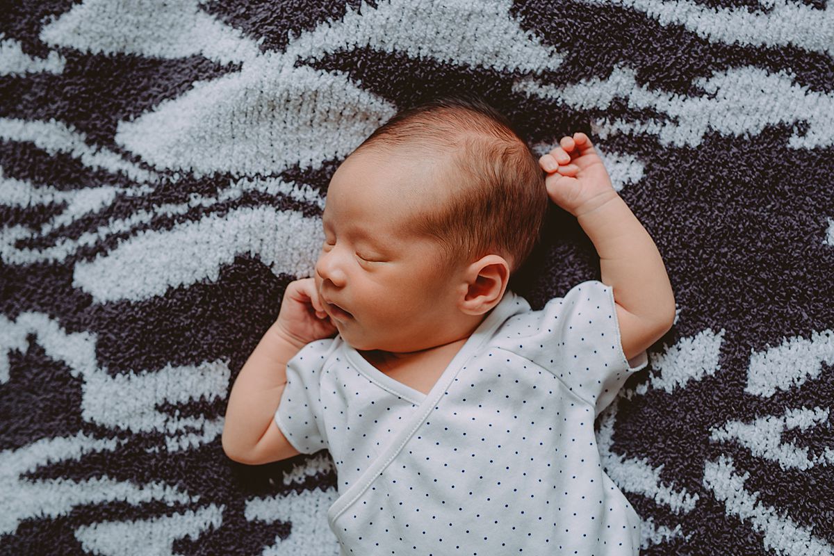 newborn laying on bed on black and white rug during nyc family lifestyle session