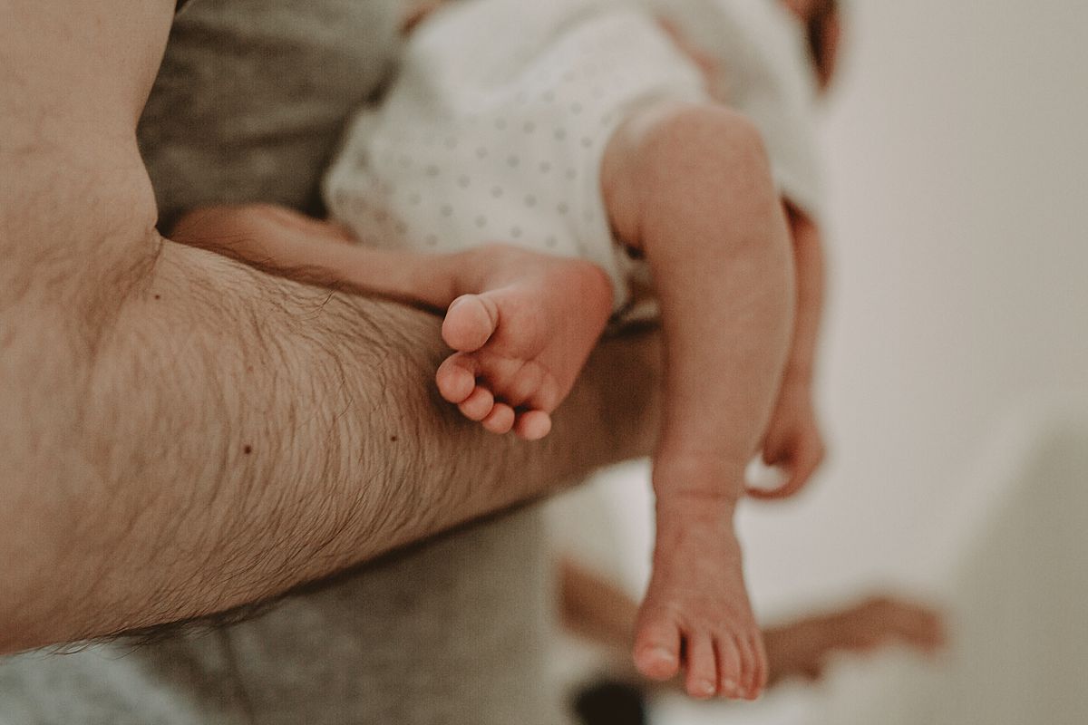 close up of newborn feet as son is straddled across dad's arms in downtown nyc apartment