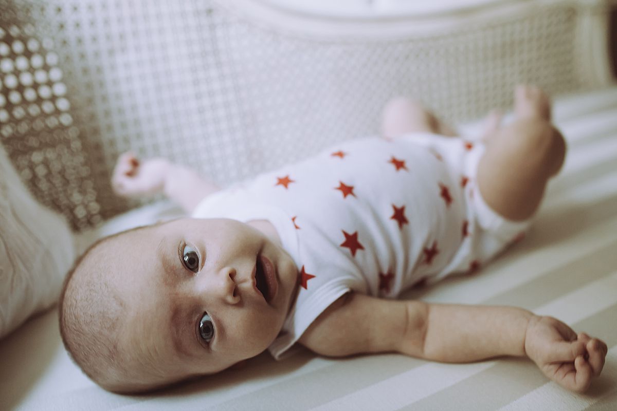 newborn girl in white and red star onesie looking right at the camera while laying near window