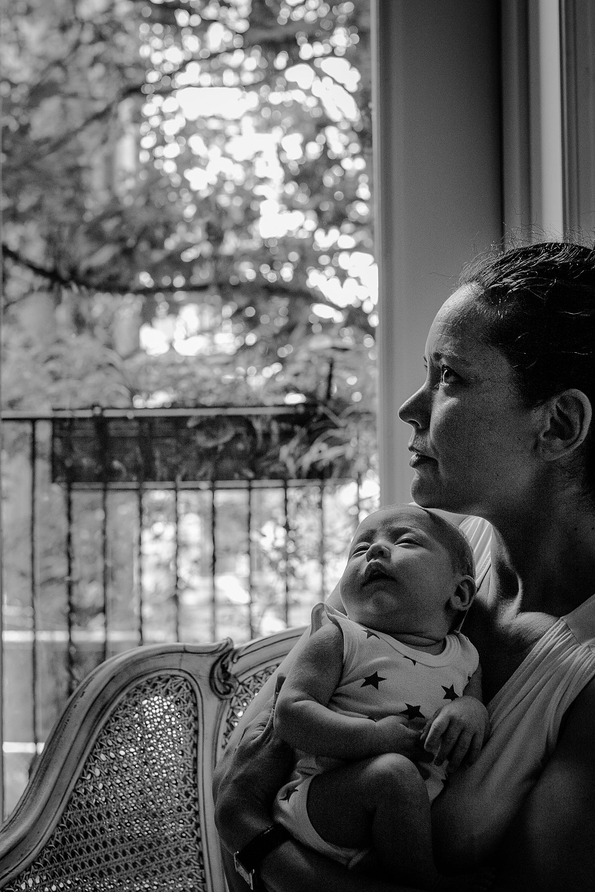 mom holds newborn sleeping newborn girl while peacefully sitting on couch during family lifestyle session in harlem nyc. image by krystil mcdowall