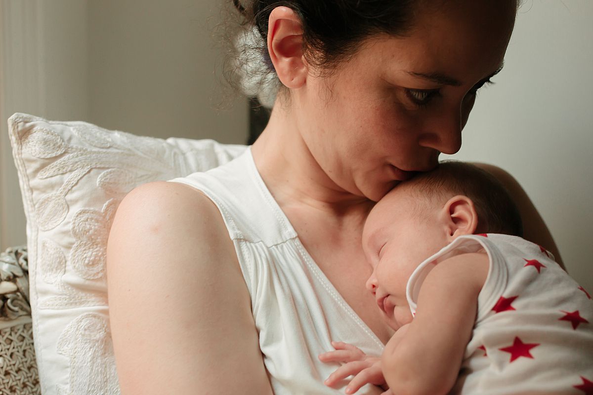 mom kisses newborn daughter while sitting outback during family lifestyle session. photo by nyc family and newborn photographer krystil mcdowall
