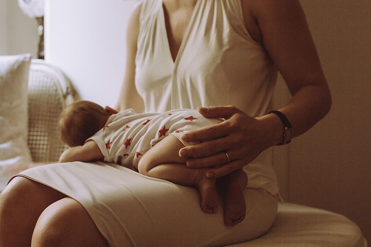 newborn baby girl sleeping on mom's lap near couch enjoying dim light. image by nyc family photographer krystil mcdowall