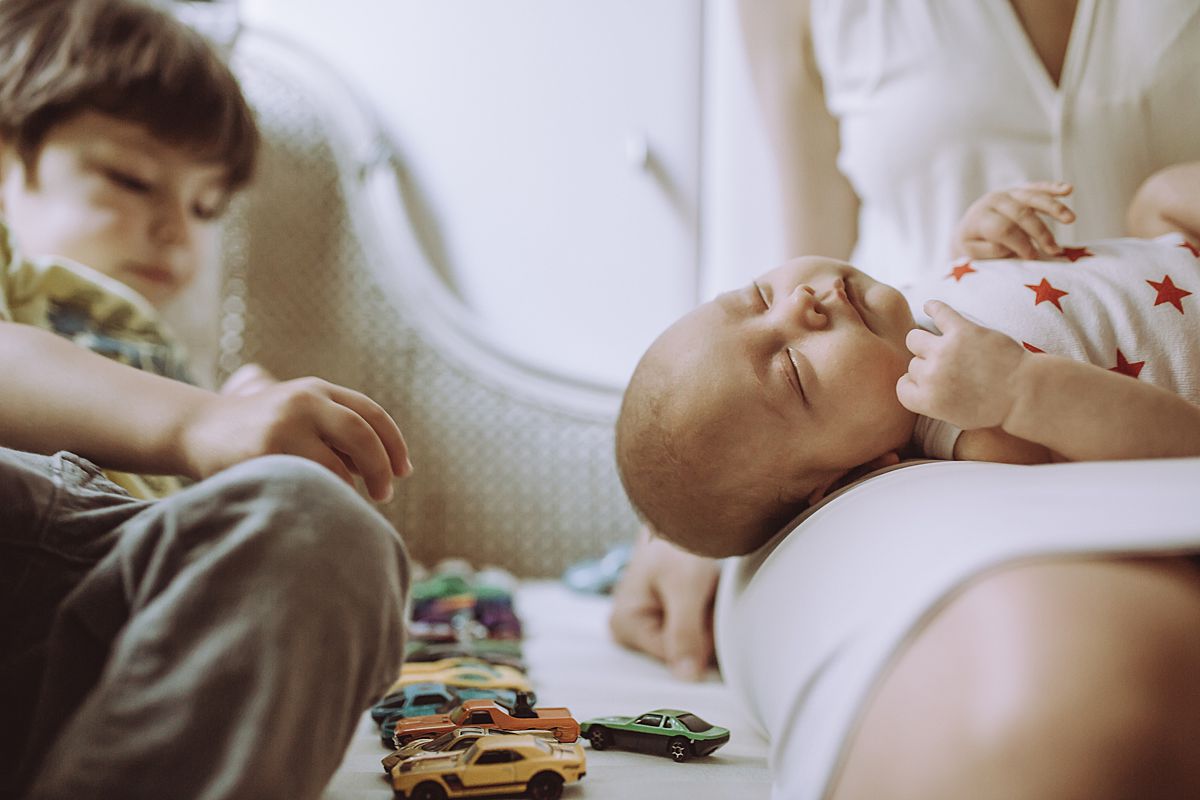 son playing with cars on couch while newborn baby girl laying on mom's lap. image by nyc family and newborn photographer krystil mcdowall