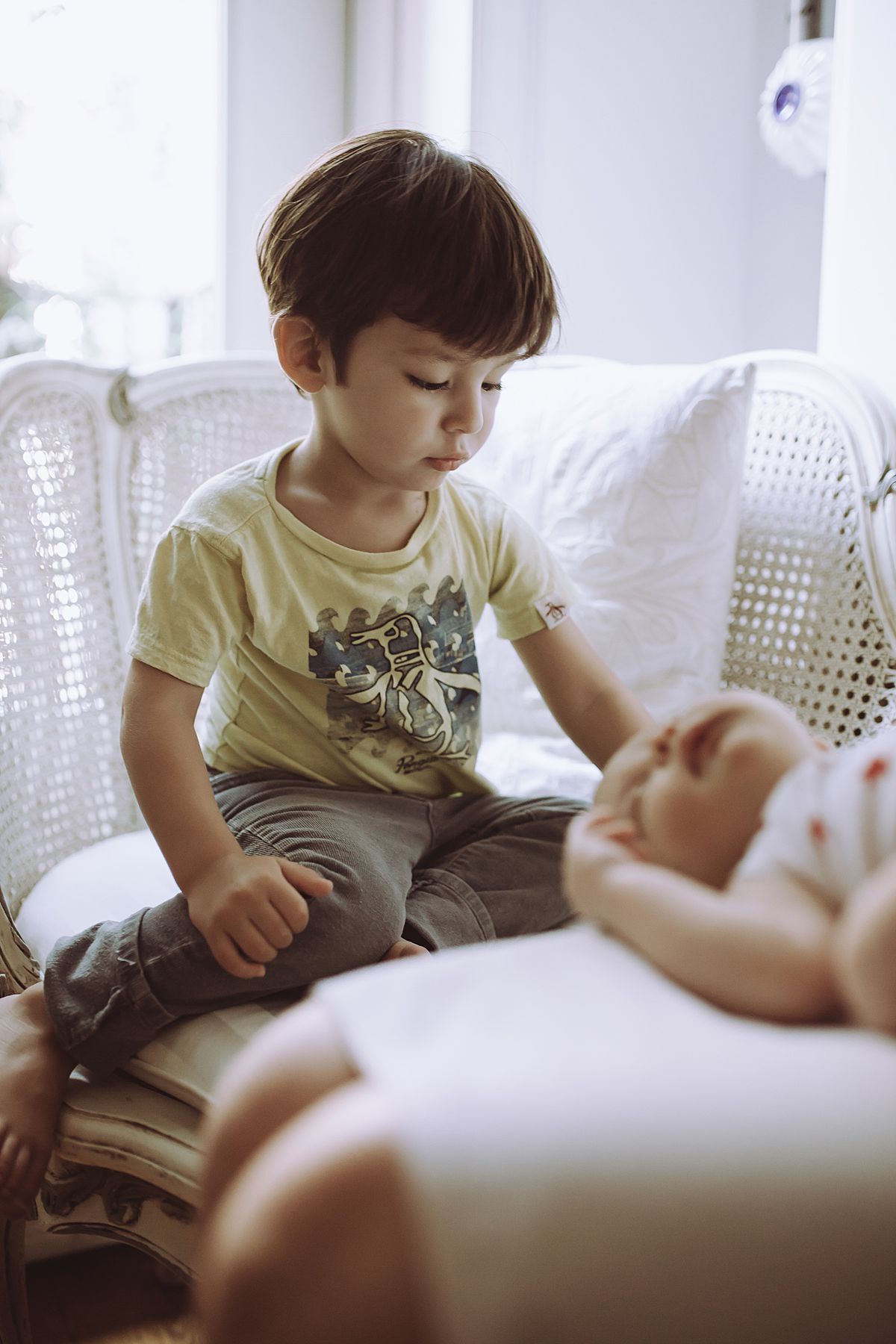 colorful image of newborn baby girl sleeping next to older brother playing with toy cars on family couch. image by nyc family and newborn photographer krystil mcdowall photography