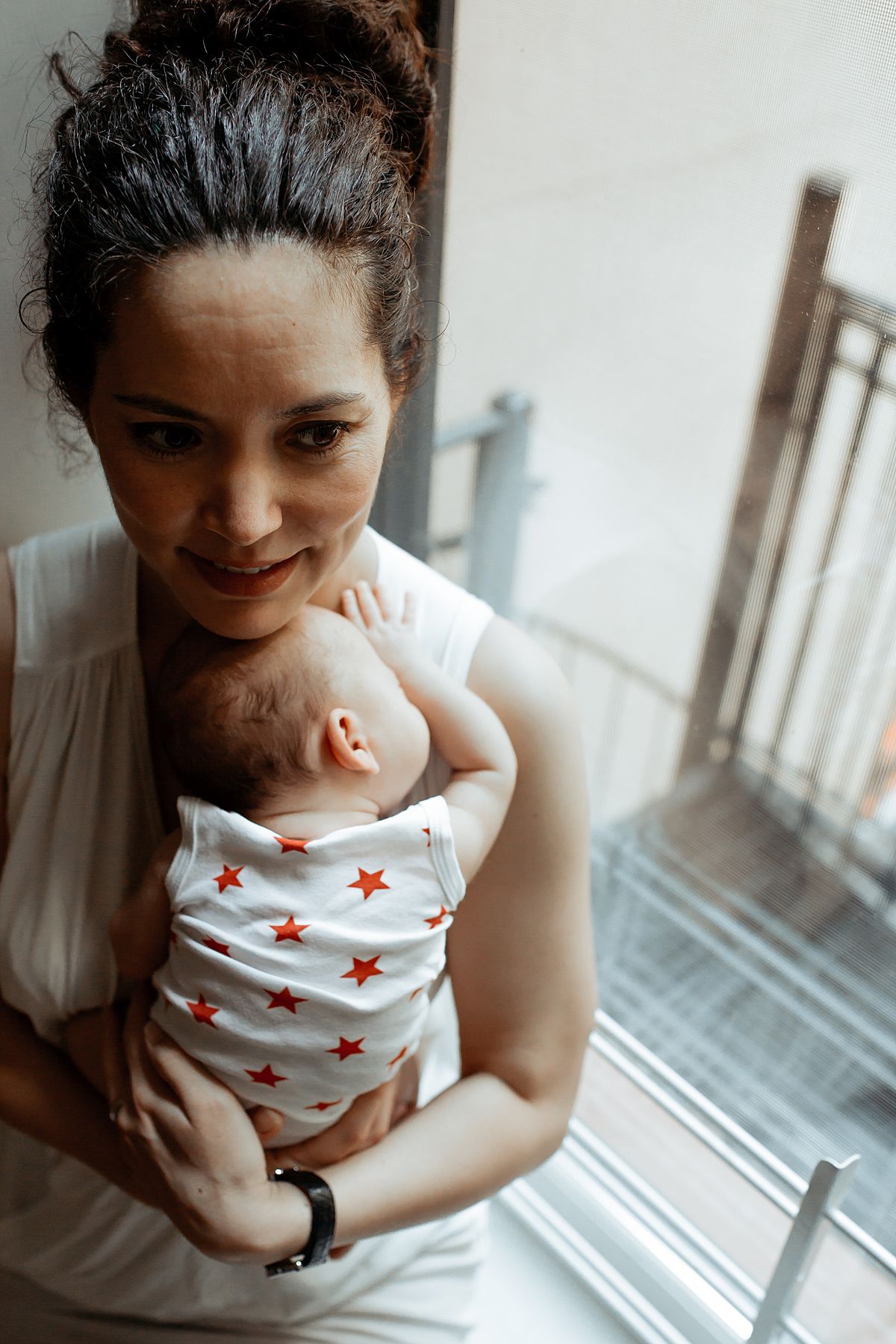 shadowy image of mom holding newborn baby girl sitting in window sill. image by nyc krystil mcdowall photography in new york city