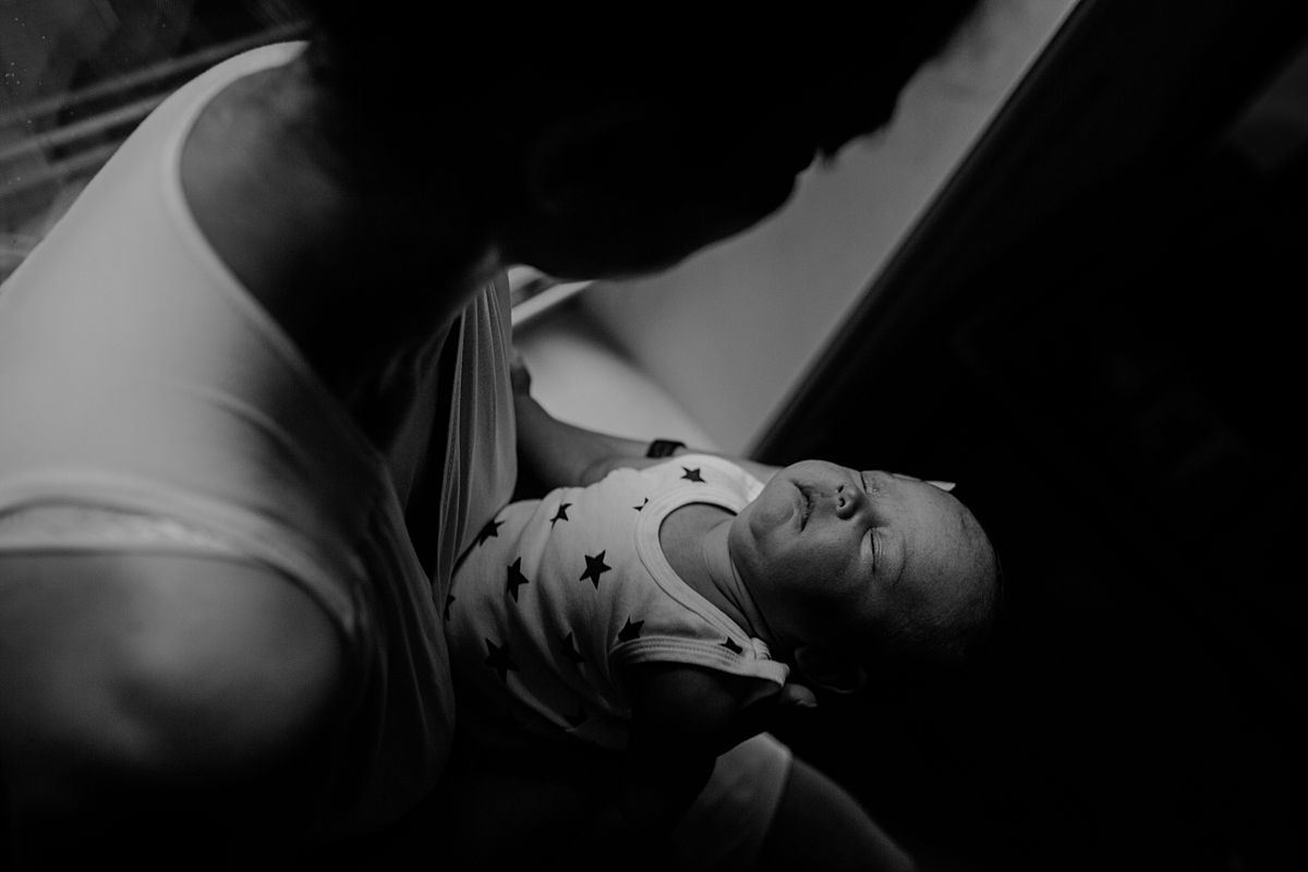 newborn baby girl sleeping outstretched while sitting in window sill with mom during lifestyle family session. photo by krystil mcdowall photography