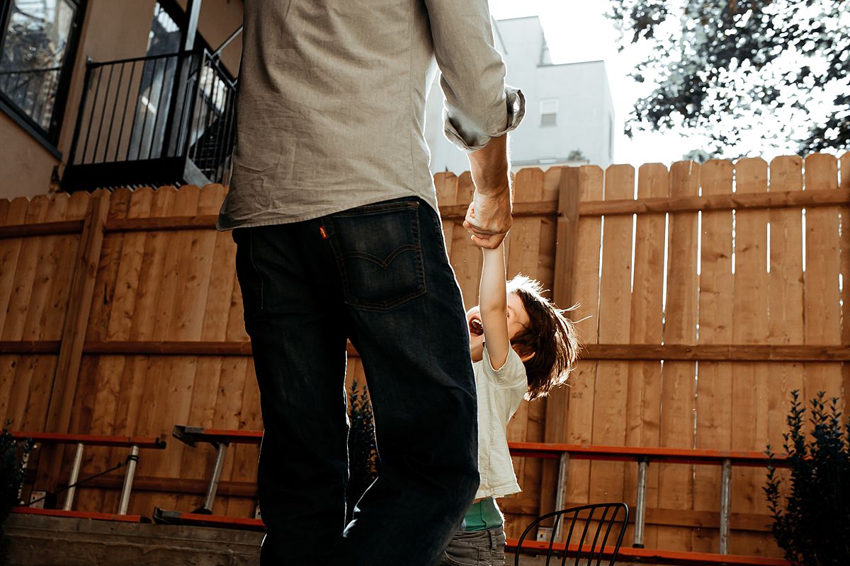 dad swings boy around in sun in family backyard during documentary family session. image by krystil mcdowall photography