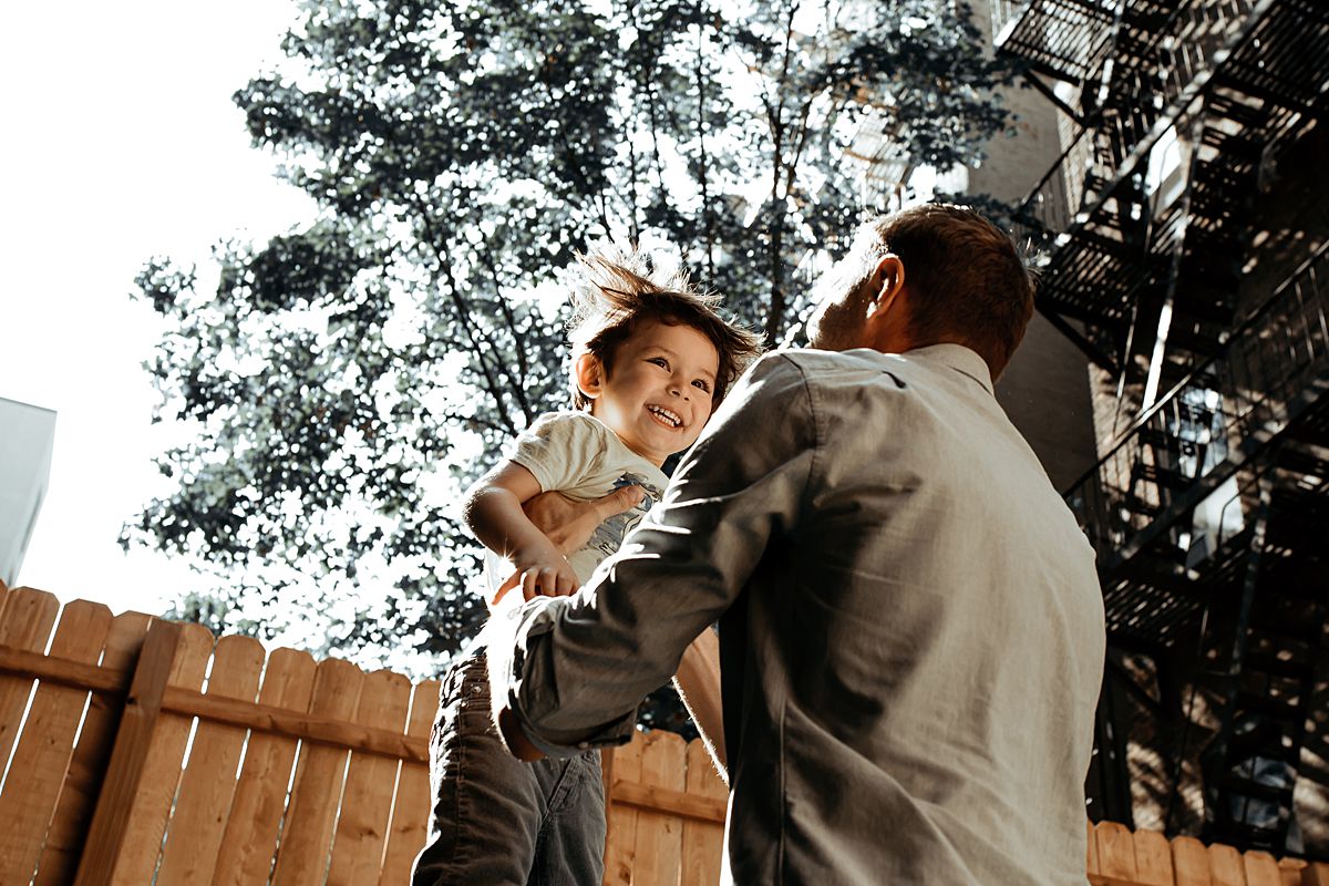 dad throws son in the air in family backyard during documentary family session. image by krystil mcdowall photography