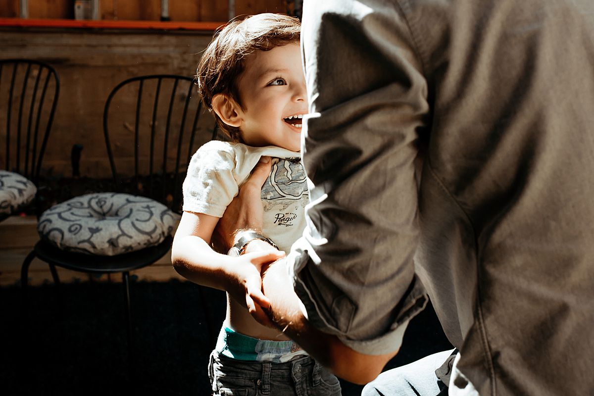 young boy smiles before dad picks him up to swing him around. photo by nyc family and newborn photographer in harlem new york