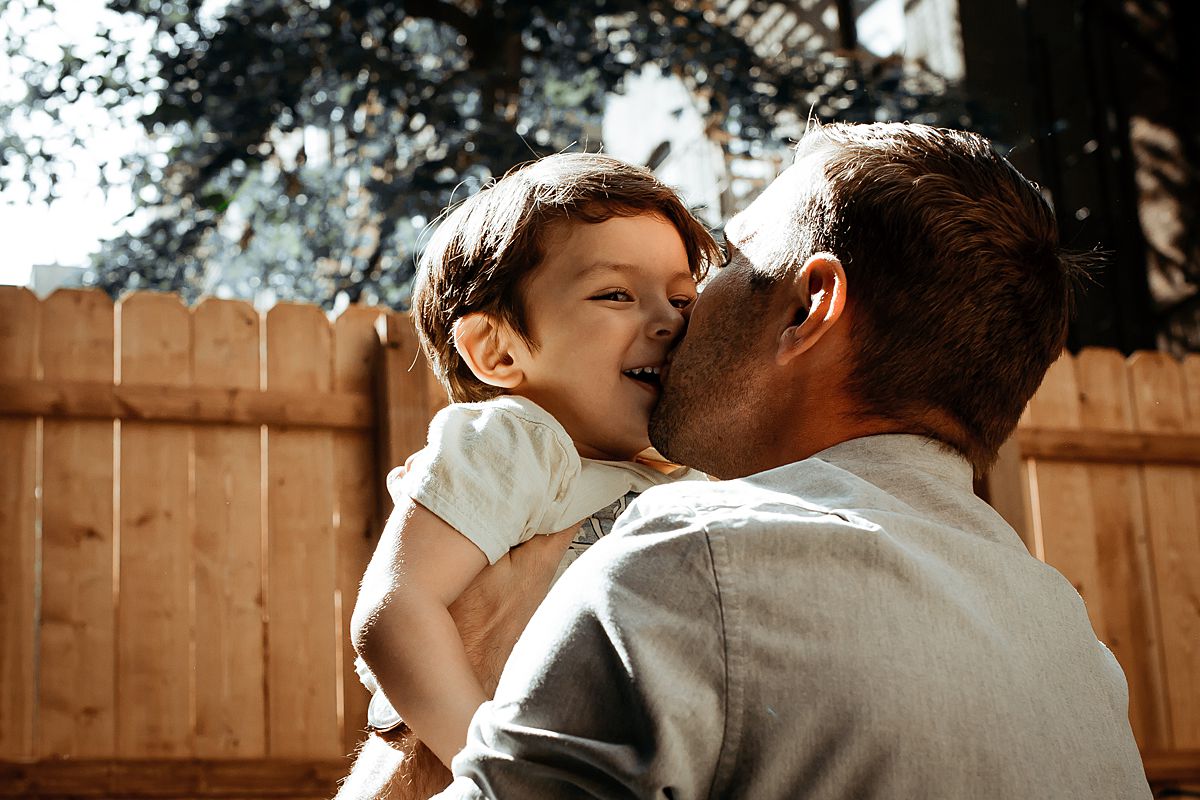 dad kisses son before he throws him in the air during documentary family session. photo by krystil mcdowall