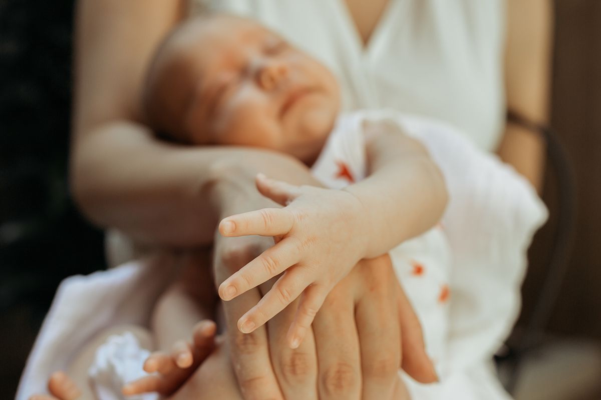 newborn daughter cuddles up to mom while sitting outback during family lifestyle session. photo by nyc family and newborn photographer krystil mcdowall