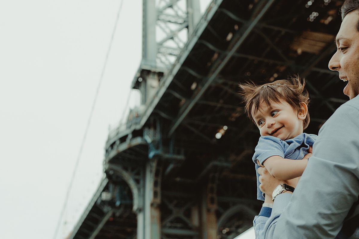 dad holds son in front of manhattan bridge in dumbo during fun family sessions. photo by krystil mcdowall photography