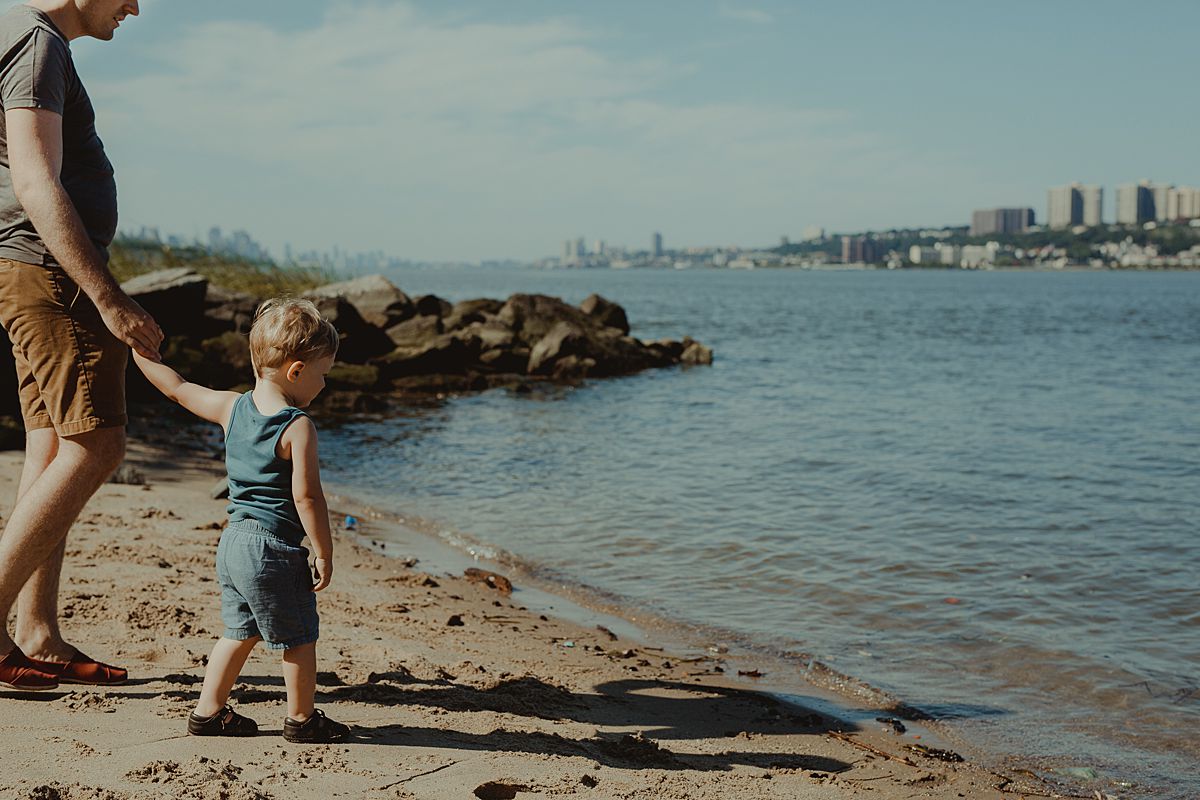 dad and toddler son exploring the hudson river from upper manhatttan during candid family lifestyle session with krystil mcdowall