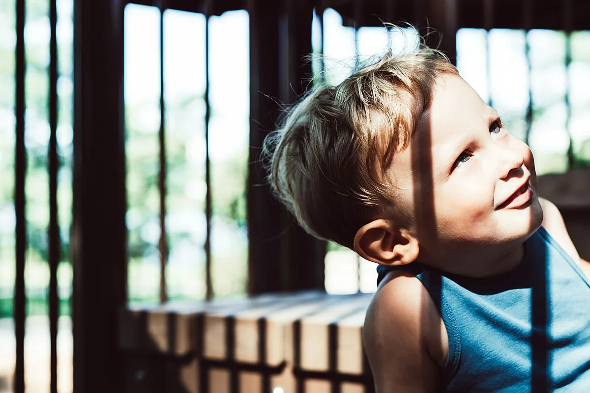toddler in discovery playground in nyc caught amongst pockets of sun and shade and looking up playfully in nyc family lifestyle session 