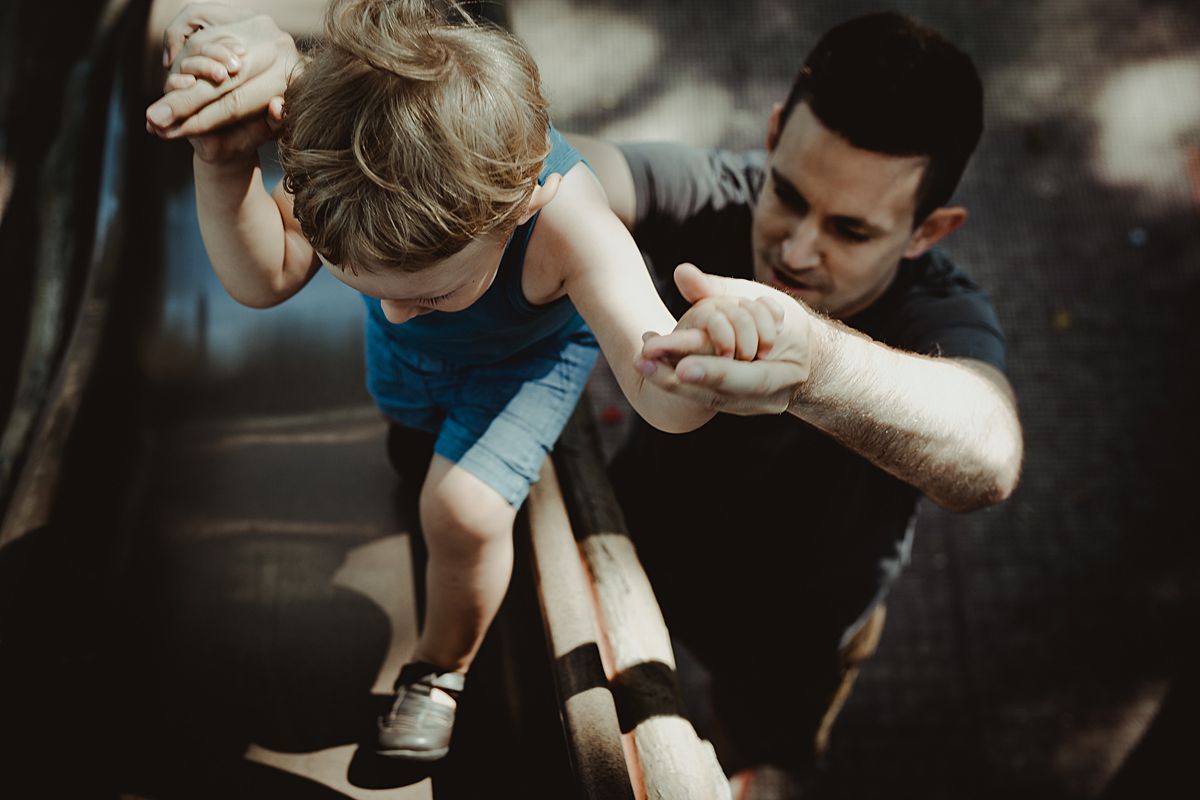 dad and son having fun at the playground with dad helping son up the slide. photo by nyc family and newborn photographer krystil mcdowall