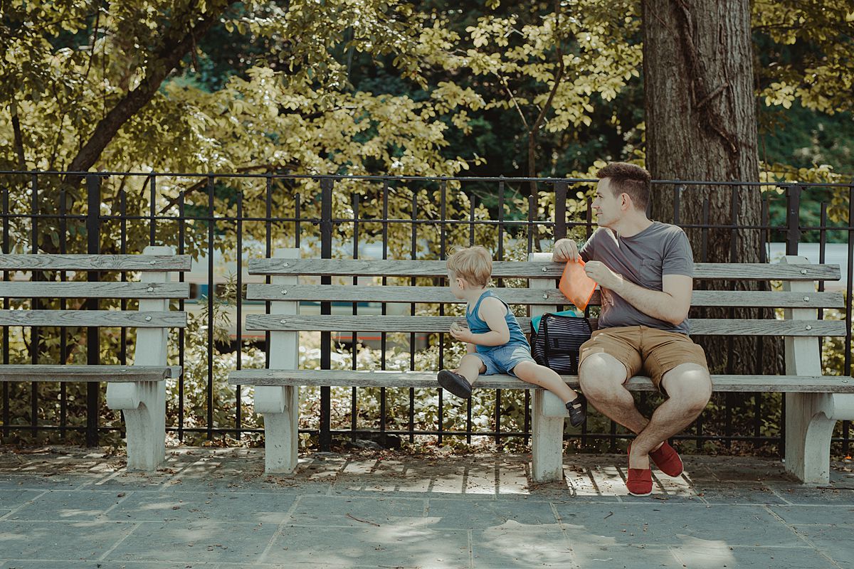 dad and son stop for a rest and a snack on nyc park bench during documentary family photo session with krystil mcdowall
