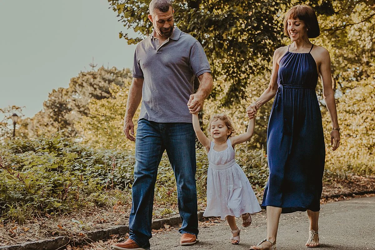 mom and dad swing daughter among fall leaves in the park during candid family session with photographer krystil mcdowall