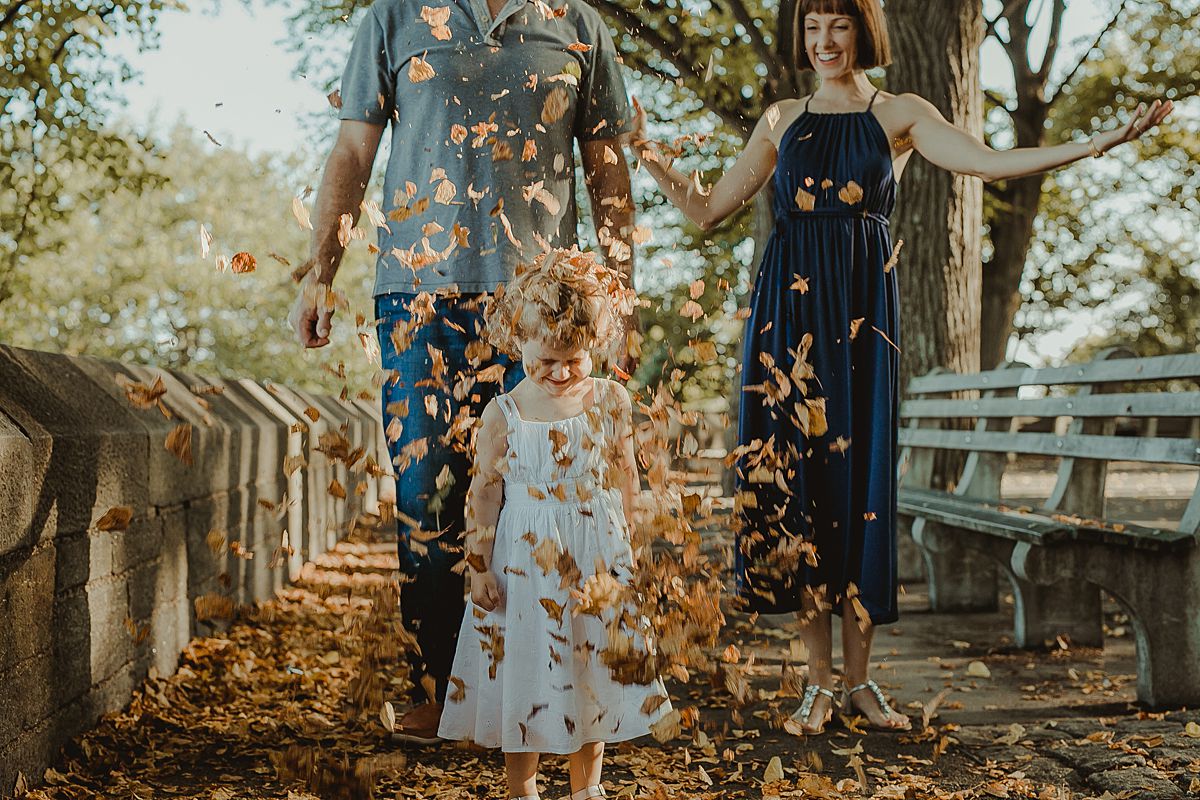 mom and dad throw fall leaves over daughter in candid family session in nyc. photo by krystil mcdowall photography