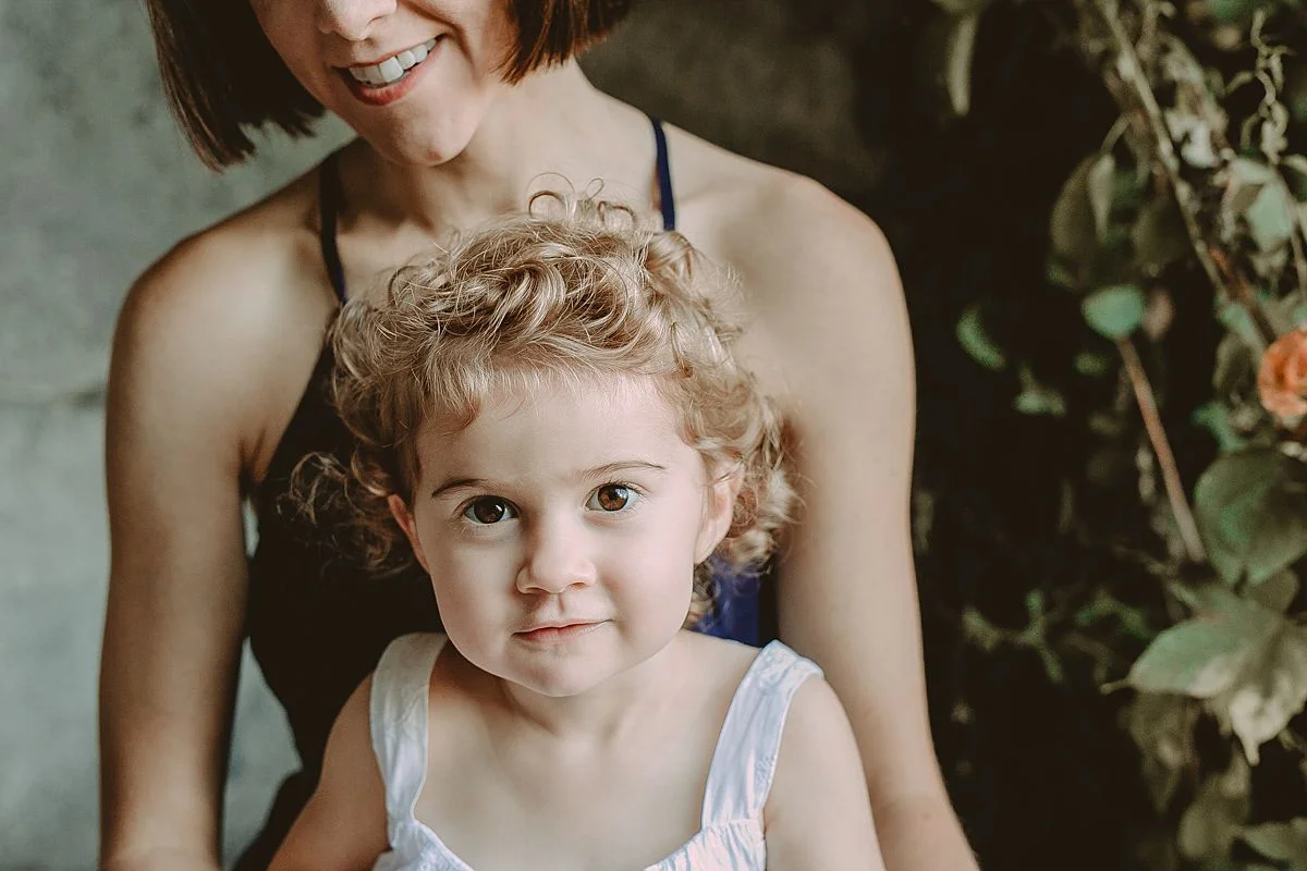 daughter sits on mom's lap in concrete park arches. photo by nyc family and newborn photographer krystil mcdowall