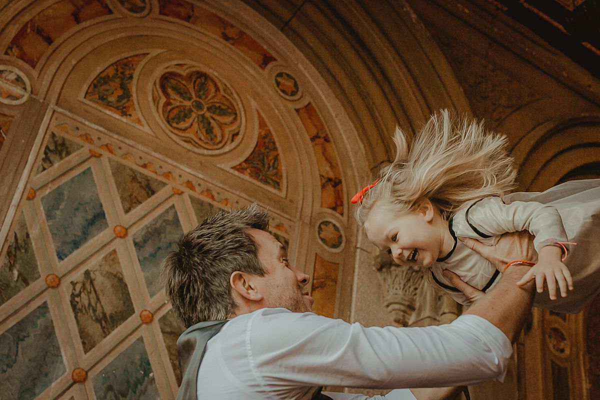 candid photo of dad throwing daughter in the air at bethesda terrace in central park. image by nyc family photographer krystil mcdowall