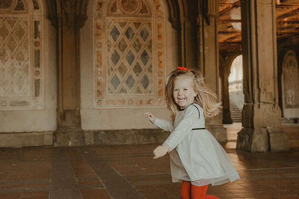 candid playful photo of young girl running around laughing at bethesda terrace in central park nyc. image by krystil mcdowall photography