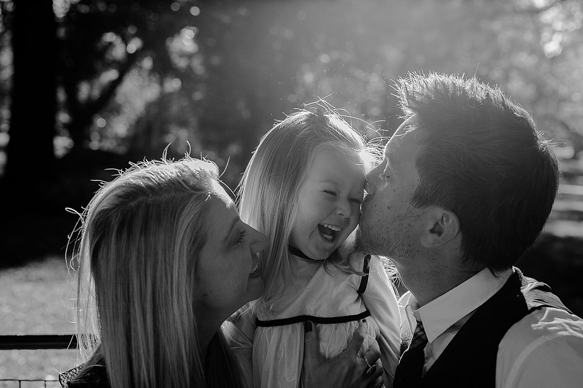 daughter, mom and dad enjoy laughter and cuddles on park bench in nyc. image by nyc family photographer krystil mcdowall photography