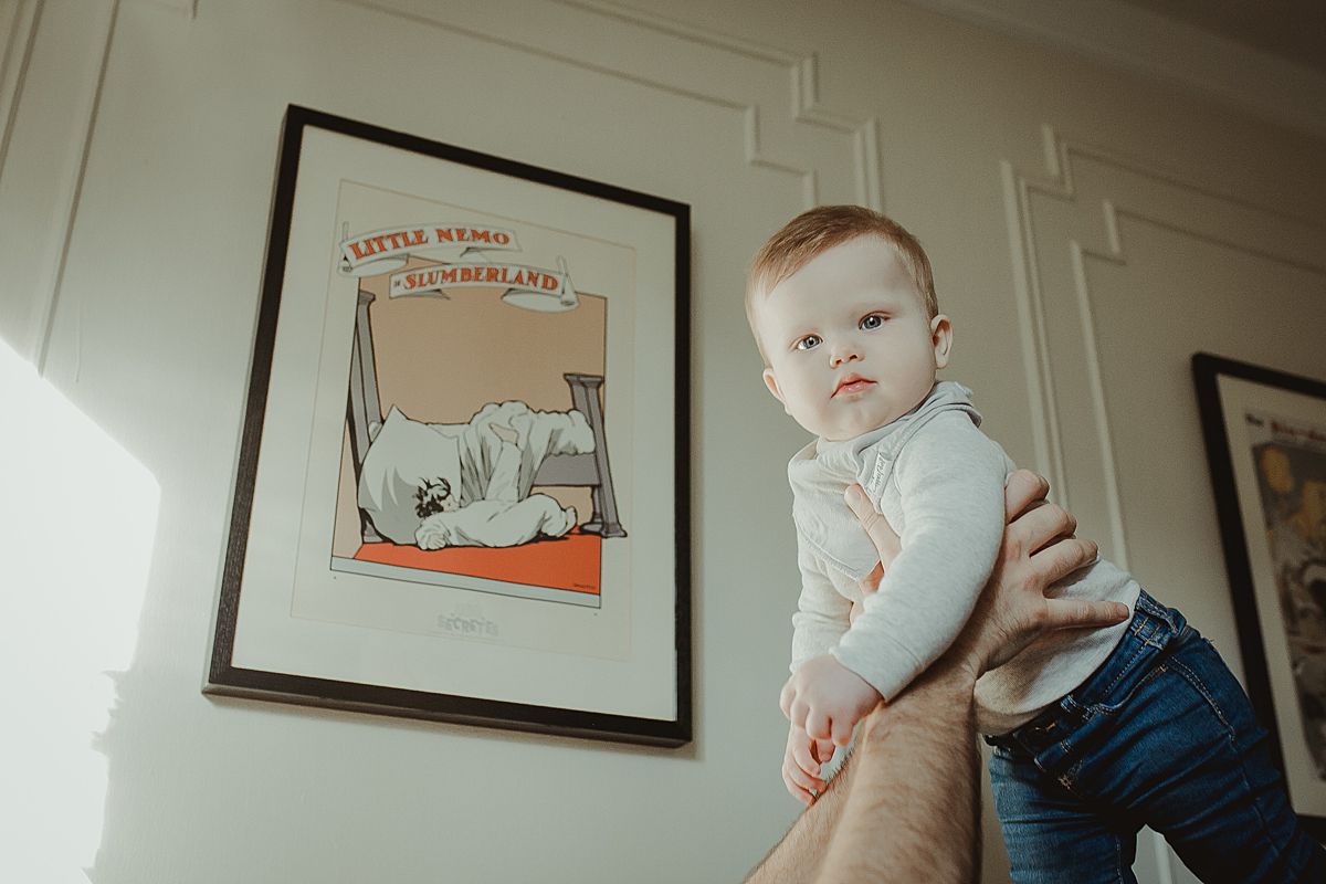 dad holds baby in the air in living room against backdrop of colorful wall hangings. krystil mcdowall photography capturing candid family photos