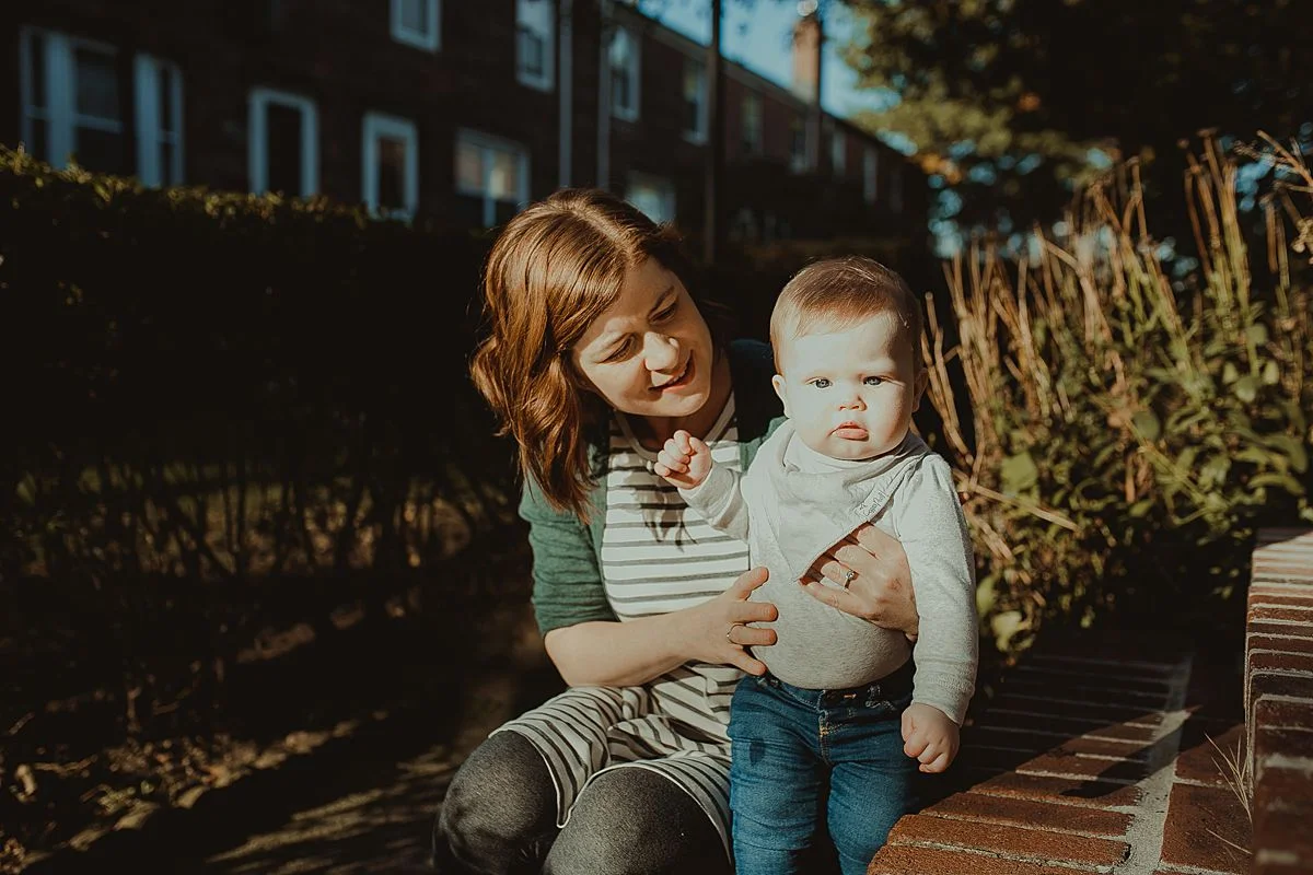 mom and son sitting enjoying the morning sun while sitting on apartment stairs during nyc family photo session. image by nyc family photographer krystil mcdowall