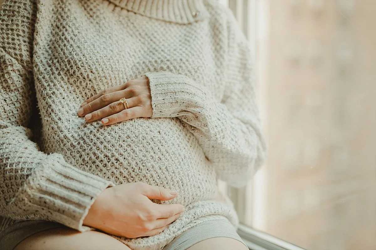close up of mom's maternity bump as she sits in light filled window of midtown nyc hotel
