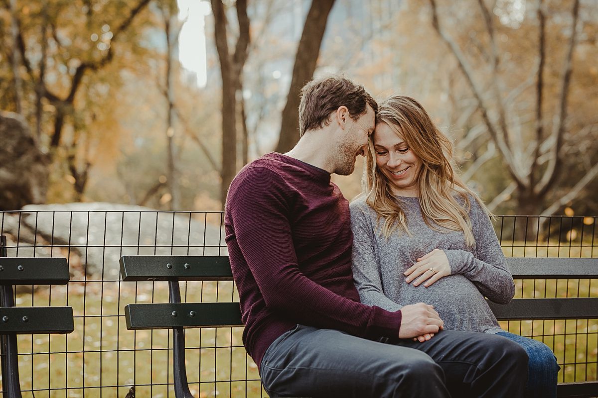 dad and mom sit on park bench in central park on beatiful fall day. image photographed by krystil mcdowall