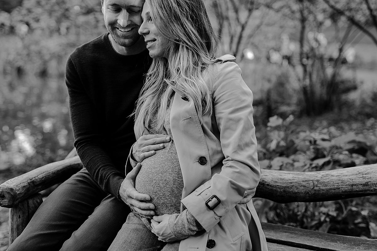 photo of husband holding wife's pregnant belly on sunny morning in central park nyc. photographed by nyc maternity photograher krystil mcdowall