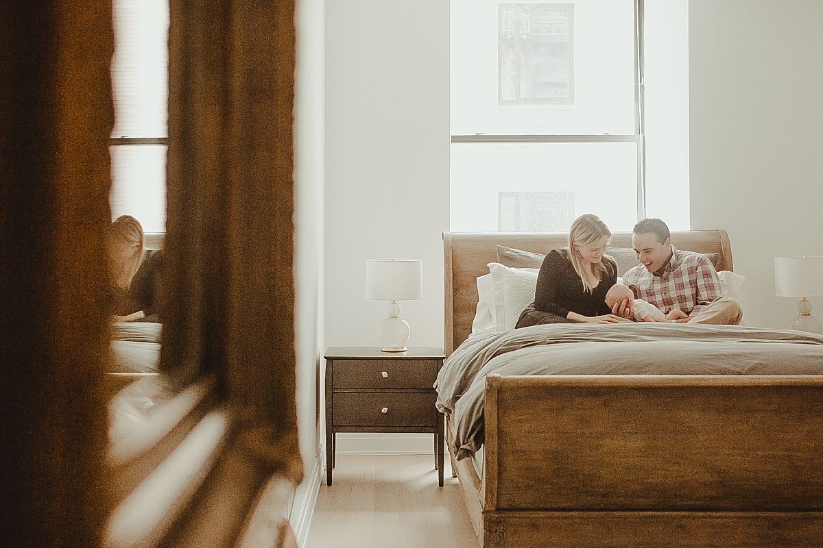 parents and newborn daughter sit on bed looking at beautiful baby girl during candid newborn session in downtown nyc. photo by krystil mcdowall photography