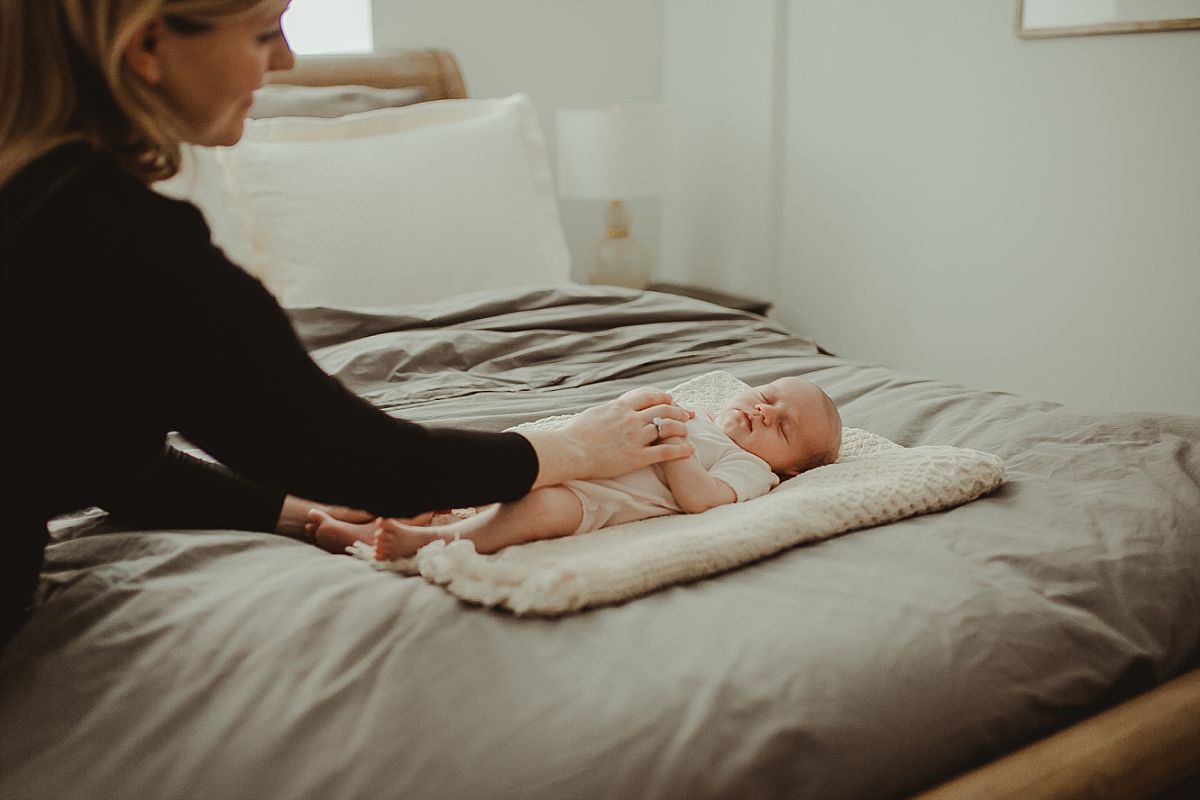 six week newborn girl sleeps on mom and dad's bed while mom reaches over to soothe her. krystil mcdowll captures candid family moments 