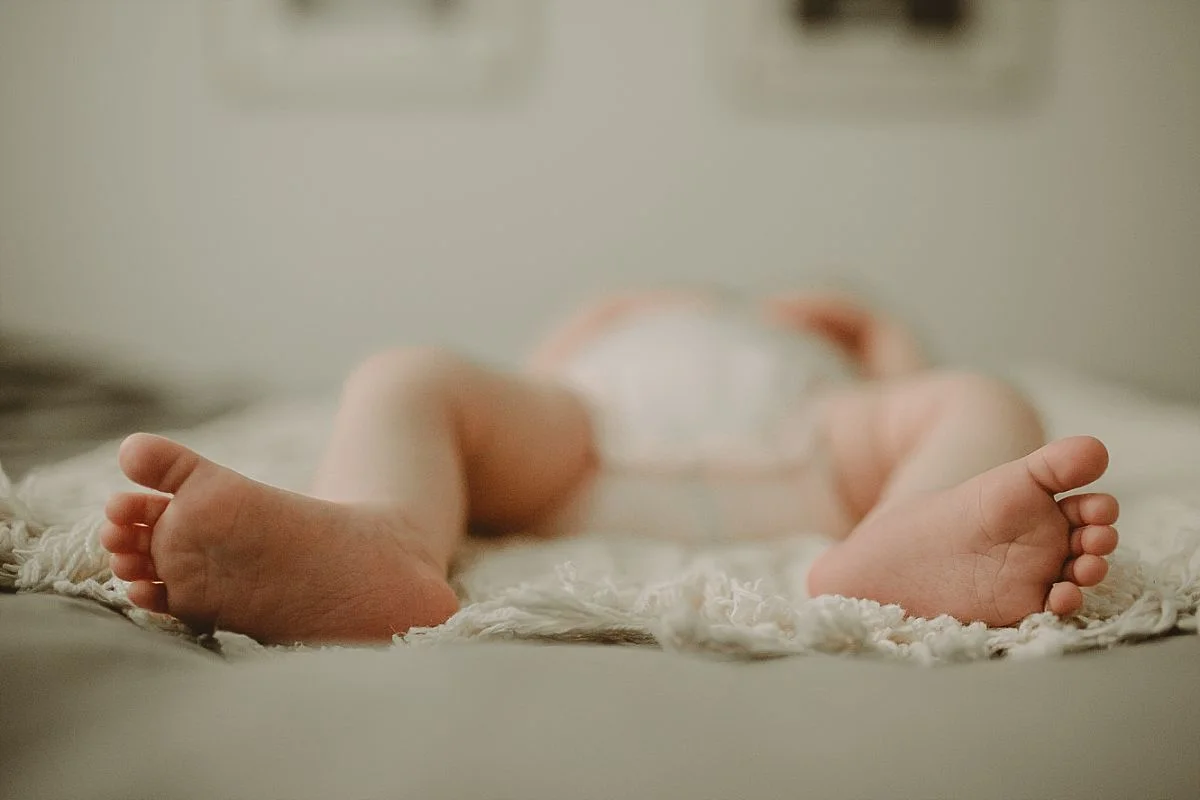 newborn portrait of baby feet while baby sleeps peacefully on parents bed. photo by krystil mcdowall photography