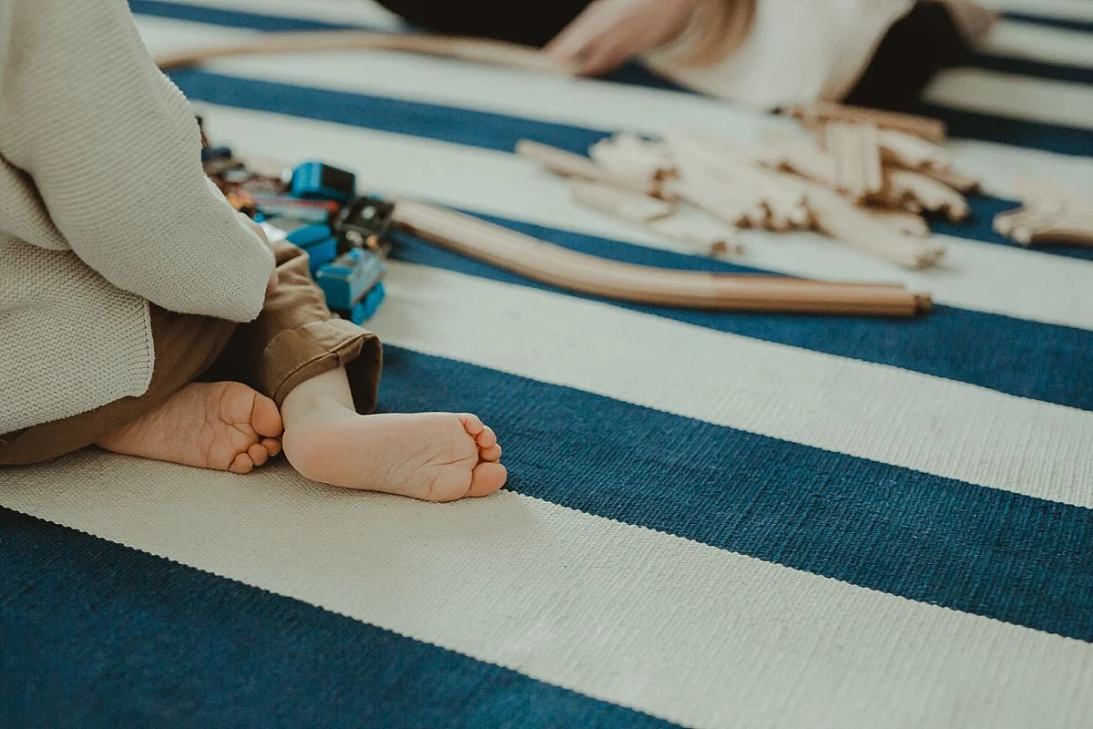 image of toddlers train set and feet while sitting on blue and white striped rug. photo by nyc family photographer krystil mcdowall
