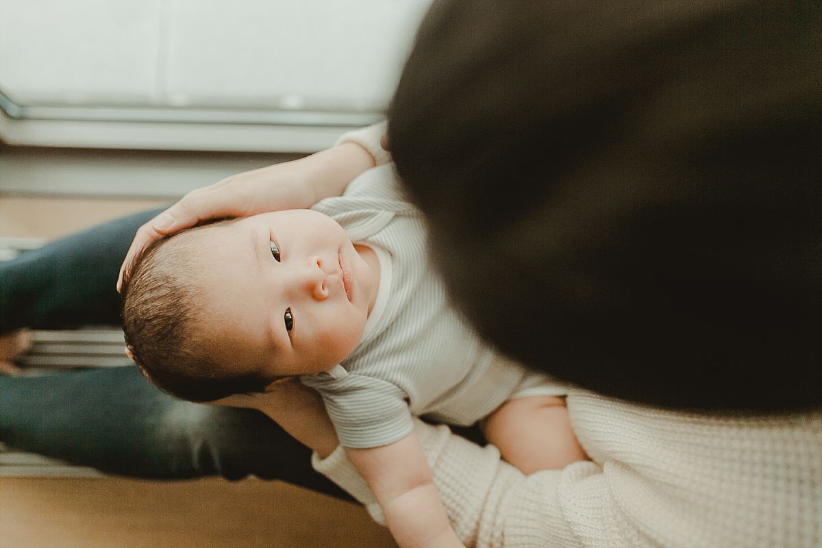 photo of newborn son sitting in mom's lap and taken from above. photo newborn baby as he lies on his blue blanket in living room of nyc apartment. photo by nyc newborn photographer krystil mcdowall