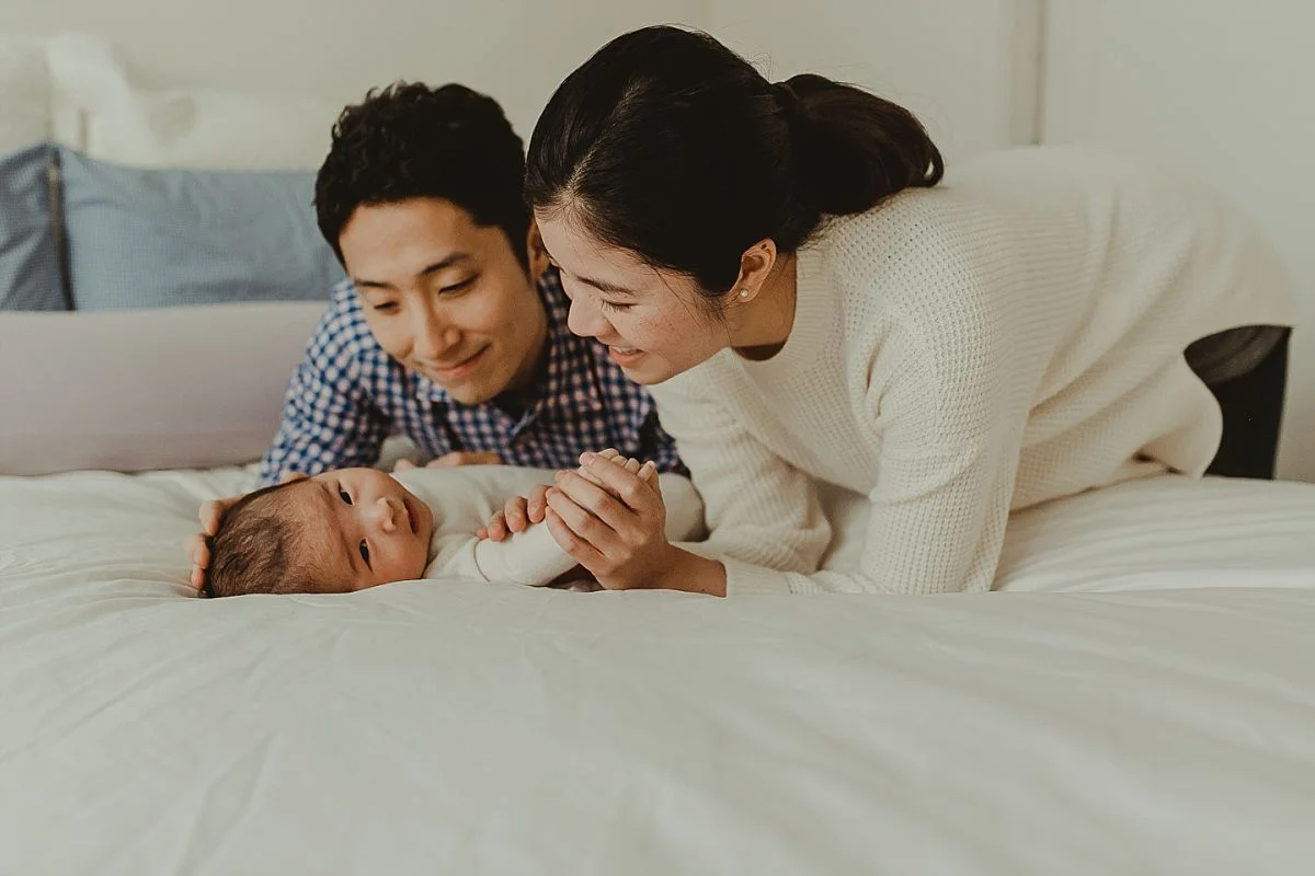 dad and mom play with newborn son on bed. photo by nyc newborn photographer krystil mcdowall