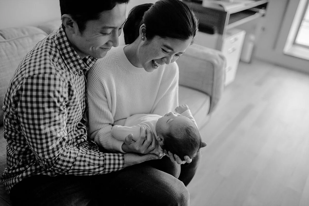dad and mom laughing with newborn son and playing on couch