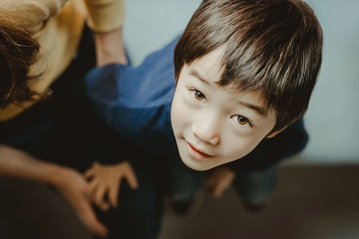 bird's eye view portrait of boy looking up at camera while sitting in his manhattan hotel while on family vacation with. krystil mcdowall photography captures candid family moments