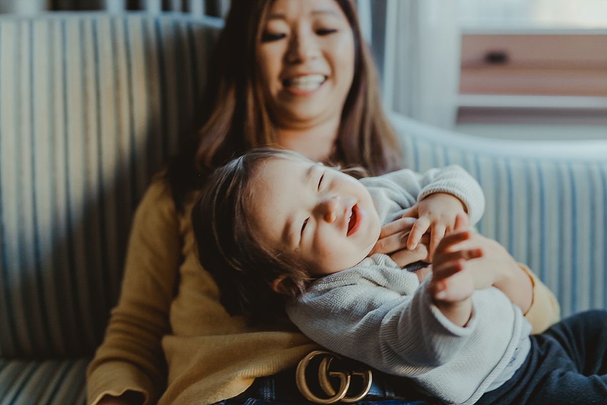 mom tickling daughter and laughing together on hotel sofa lounge during candid family photo shoot in manhattan. image by krystil mcdowall 