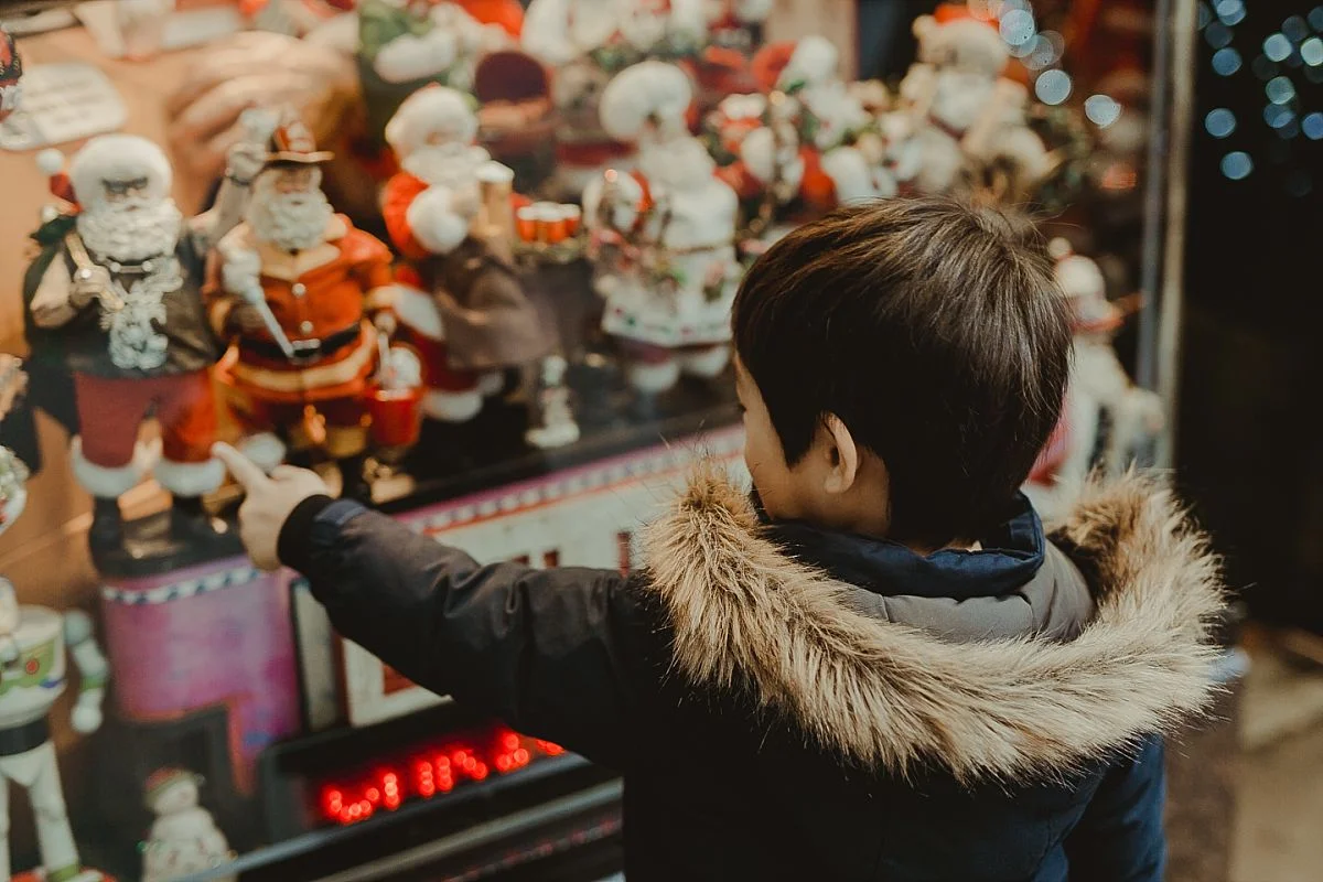 boy points at santa statues on the streets of midtown manhattan during candid family photo session in nyc. image by nyc family photographer krystil mcdowall