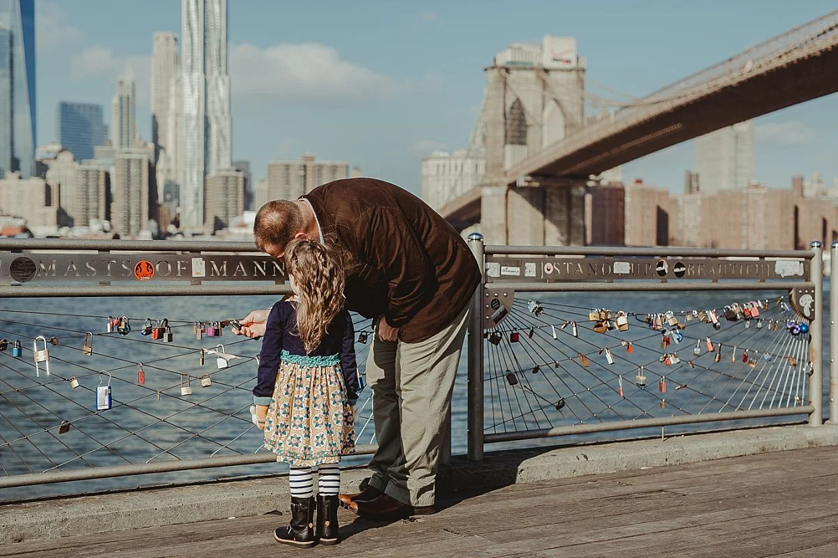 candid dad and daughter portrait as they explore the lockets at pier in dumbo brooklyn with the brooklyn bridge in the background. photo by nyc family photographer krystil mcdowall