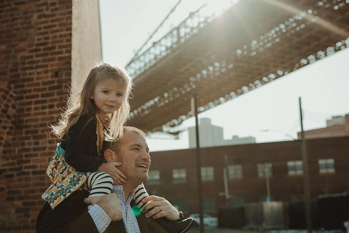 daughter gets shoulder ride from dad near the brooklyn bride in dumbo brooklyn. photo by nyc family photographer krystil mcdowall
