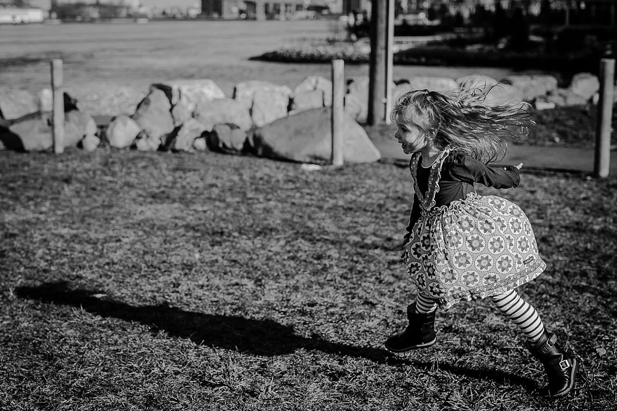 candid photo of daughter running around the grass in front of the manhattan bridge. image by nyc family photographer krystil mcdowall